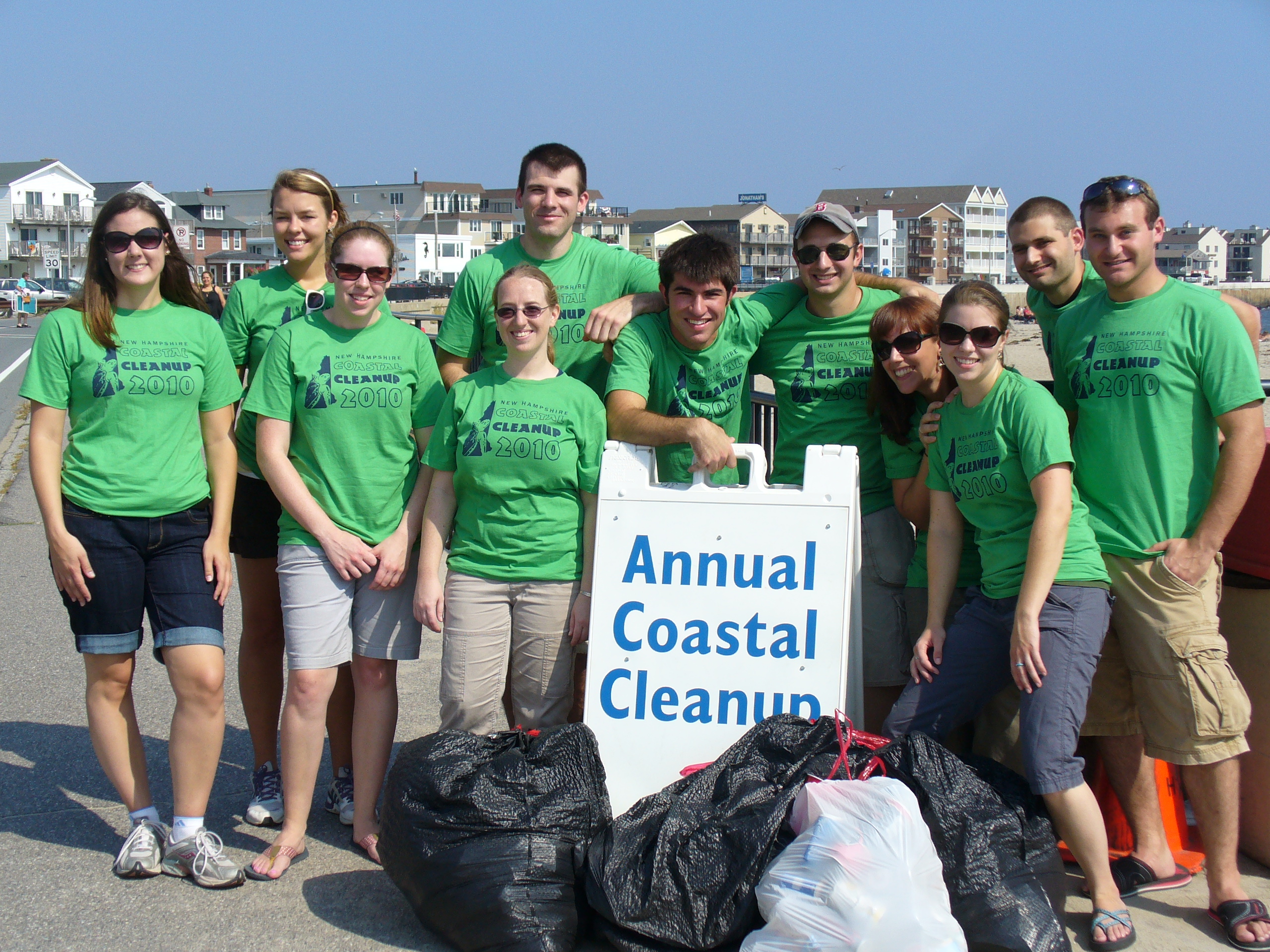 group of volunteers with full trash bags and an Annual Coastal Cleanup sign in front of them. 