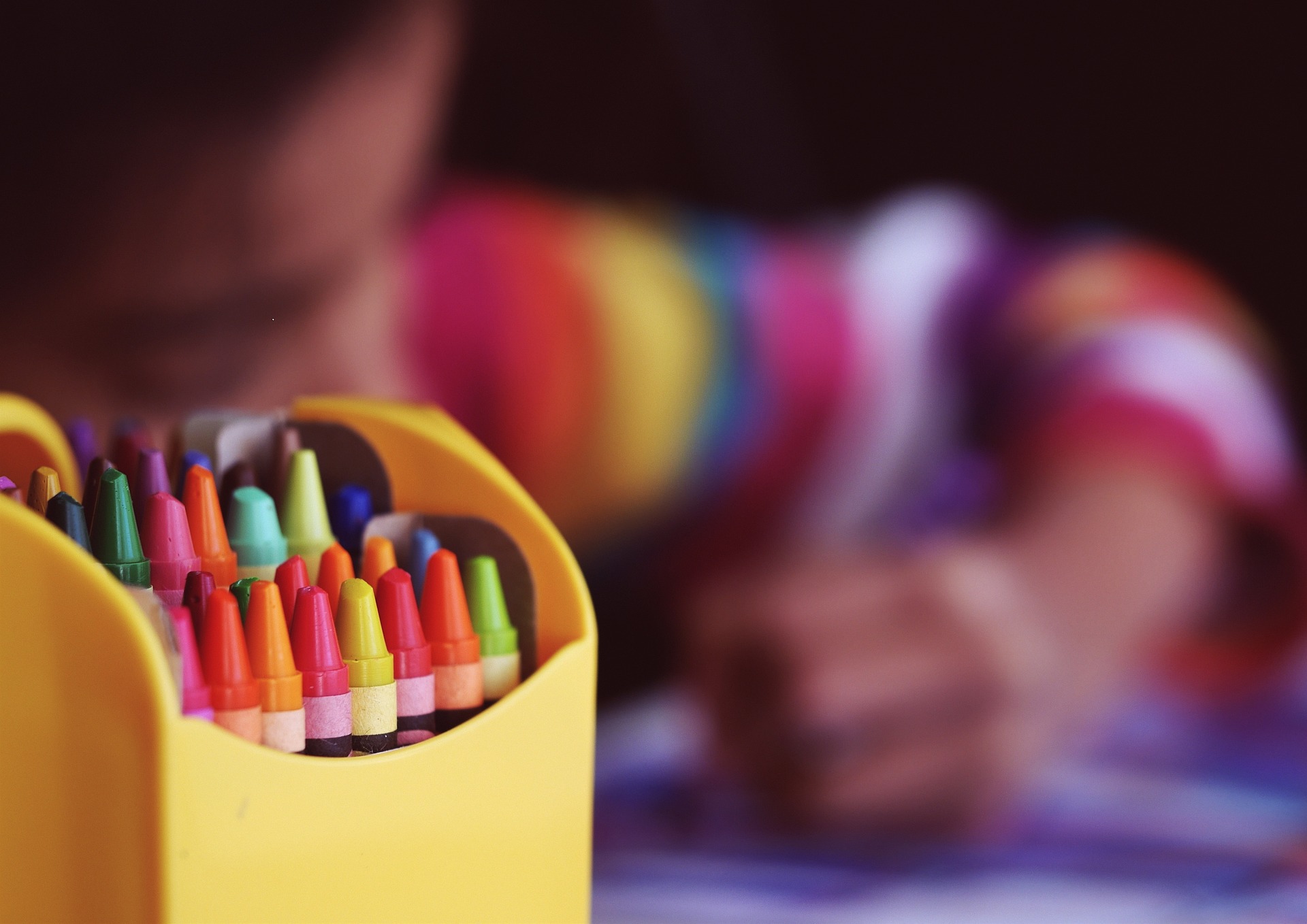 image of crayons with blurred image of child coloring in background