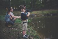 a boy stands next to a pond fishing
