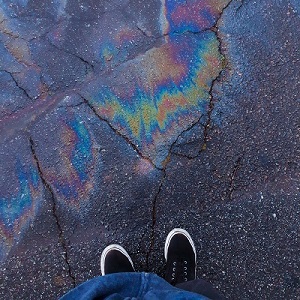A person stands in front of an oil slick on pavement