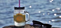 Mason jar with water and lemon slice with sunglasses; water in background.