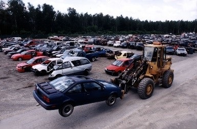  image of a vehicle being picked up by a loader at a motor vehicle salvage yard