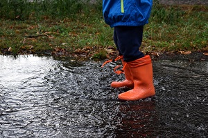 child in rain boots stands in puddle