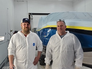 two men pose in front of a car being painted