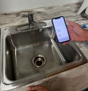 person holds a cell phone next to a sink