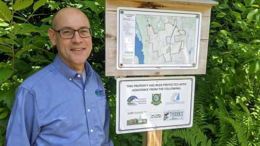 Smiling man in a blue shirt beside a sign for newly conserved land.