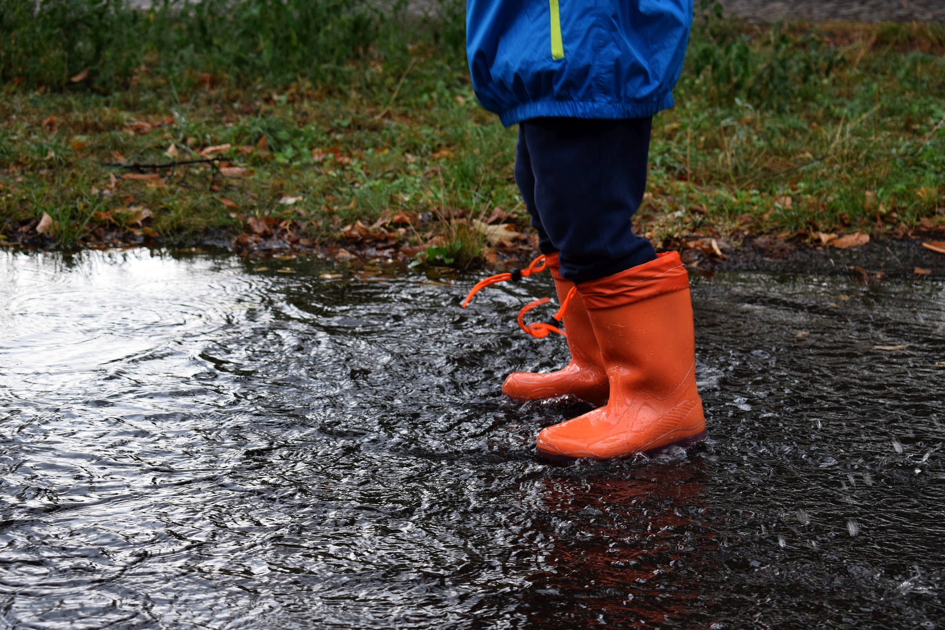 Photograph of stormwater running onto asphalt on a rainy day, with a child standing in rain gear