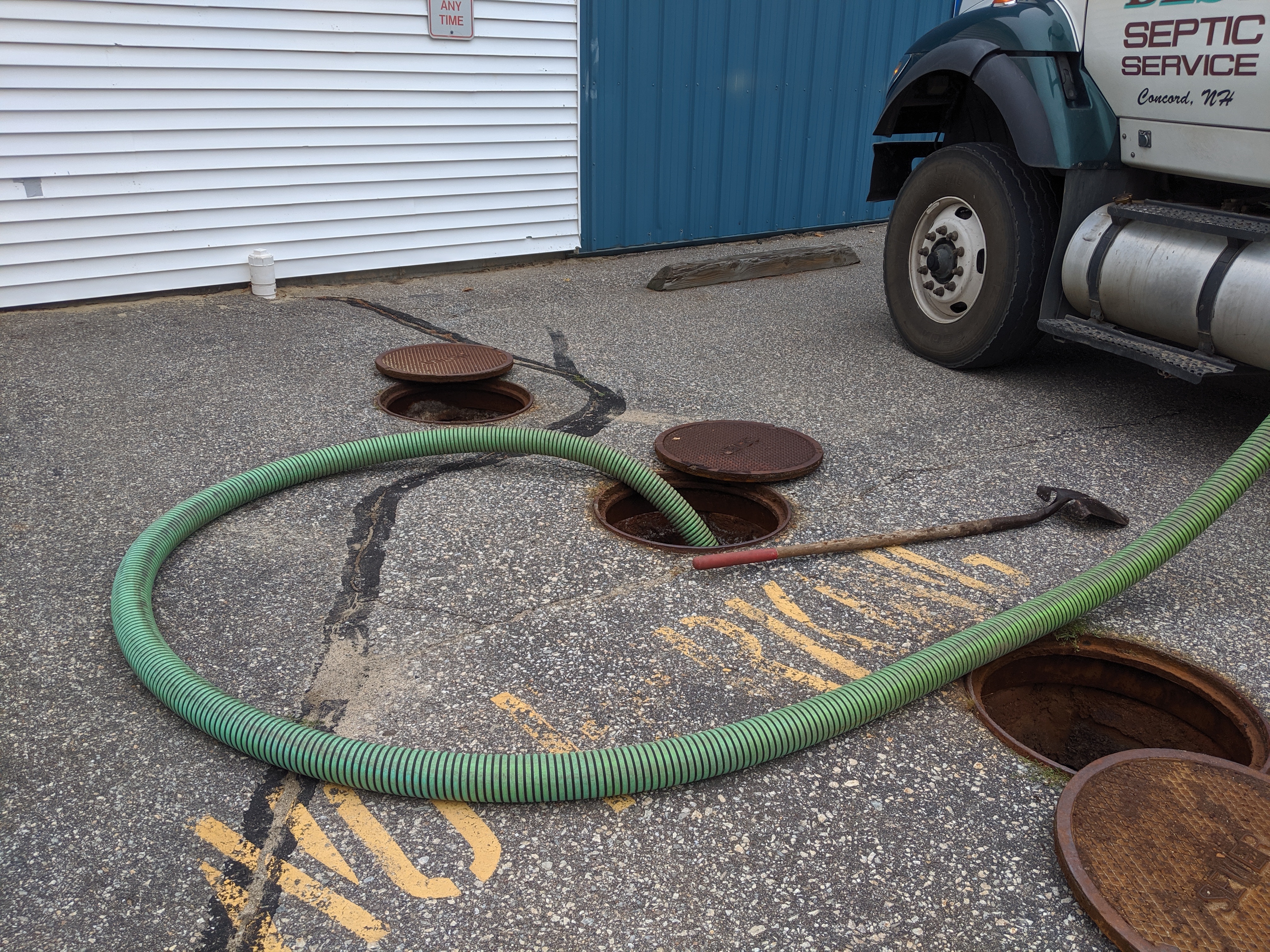 asphalt with green hose dumping the waste from a septic tank into a manhole leading to wastewater facility 