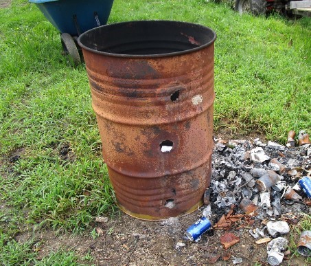 image of burn barrel with burnt trash on the ground