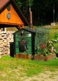  image of green outdoor wood boiler next to woodshed