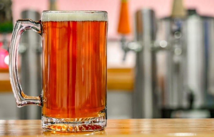 photo of a glass of beer next to brewery equipment