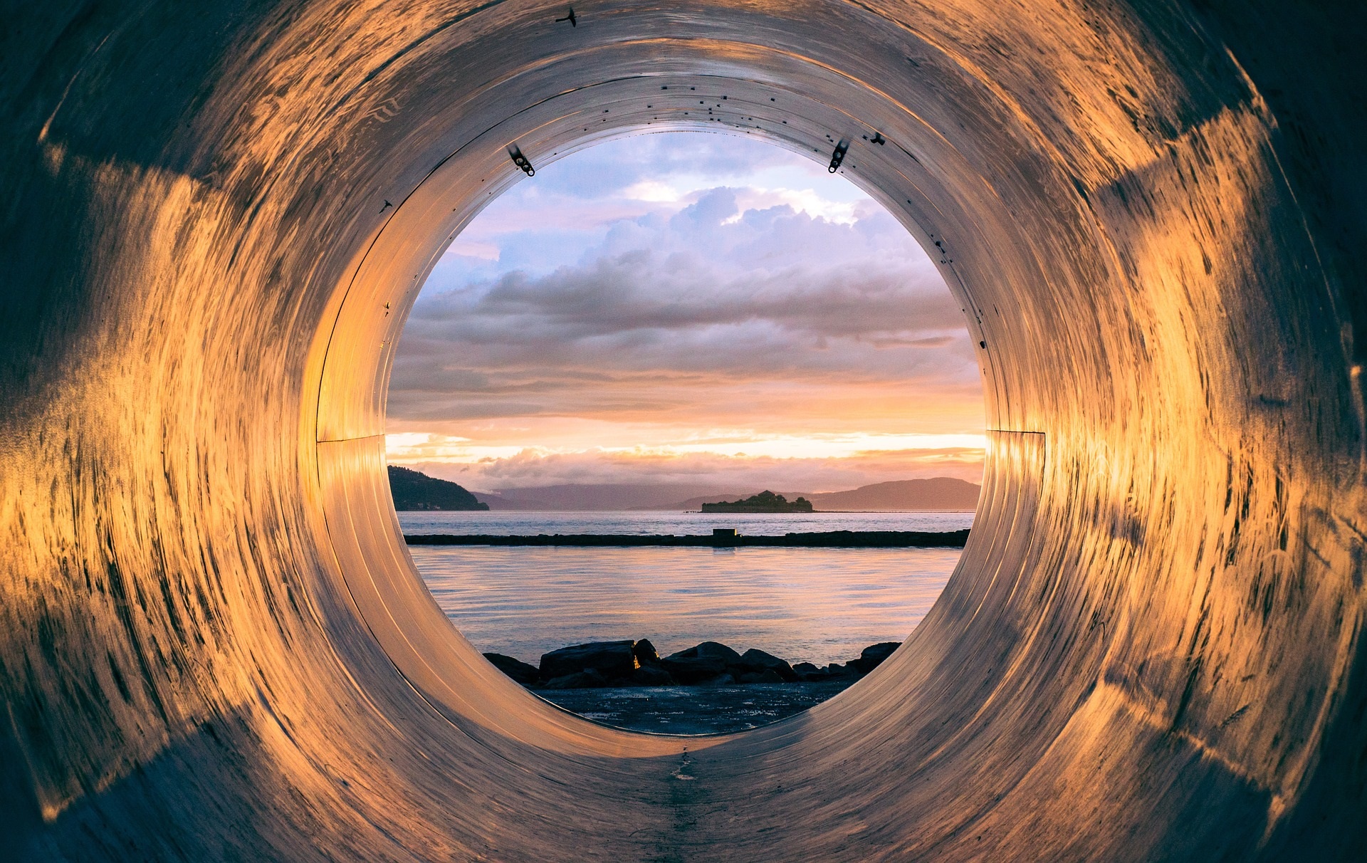 Inside of a large concrete pipe that outlets into a lake with a sunset drop.