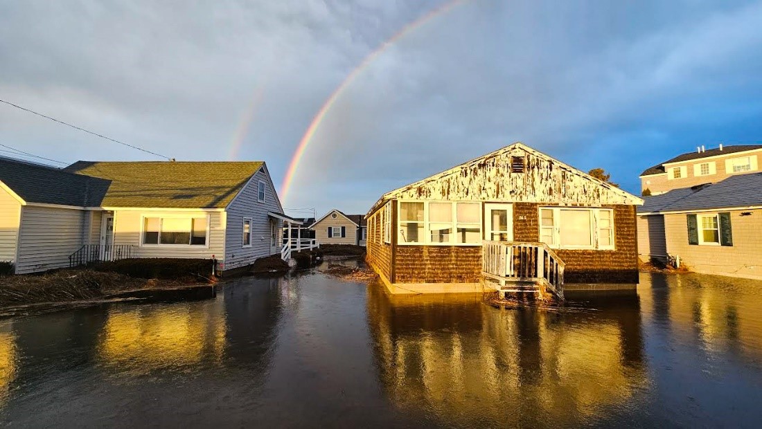Flood waters surrounding coastal houses with a rainbow overhead.