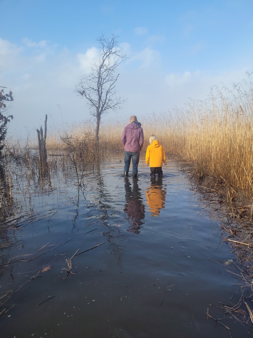 An adult and child stand together in a flooded marsh area.