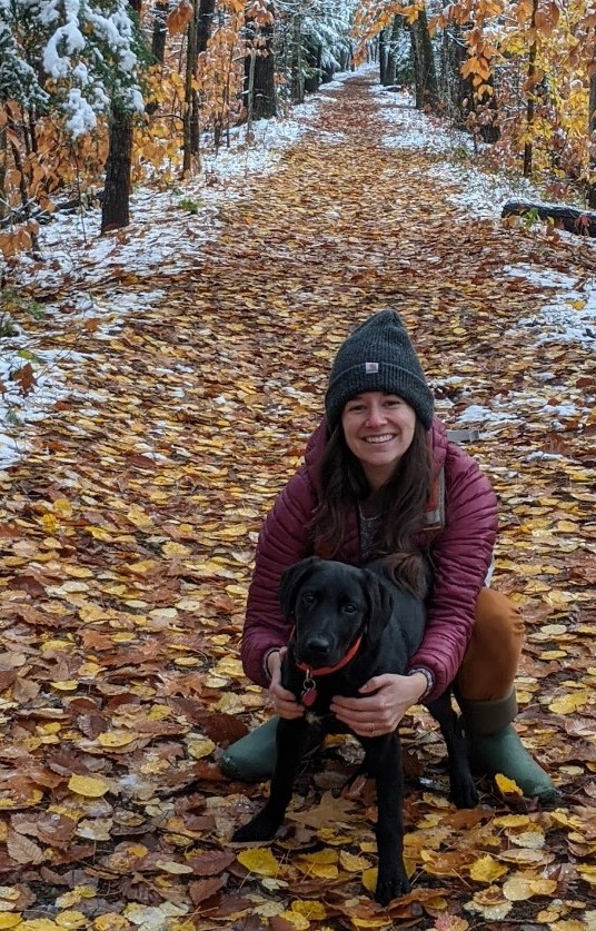 Woman on a path covered with fall leaves with a black dog.
