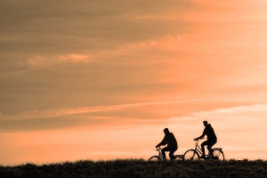 image of two cyclists riding in front of a pink sky