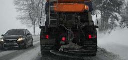 Back of road plow spreading salt as it drives down winter road.