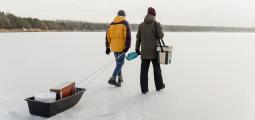 two men walk out on the ice with their fishing gear
