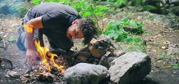 a man blows on a campfire to keep it going