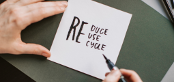 A person writes "reduce, reuse, recycle" onto a piece of paper.